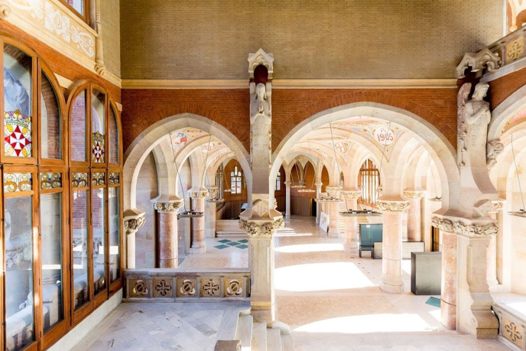 석조 아치, 기둥, 스테인드글라스 창문이 있는 화려한 인테리어. 햇빛이 들어와 복잡한 디테일을 밝힙니다.