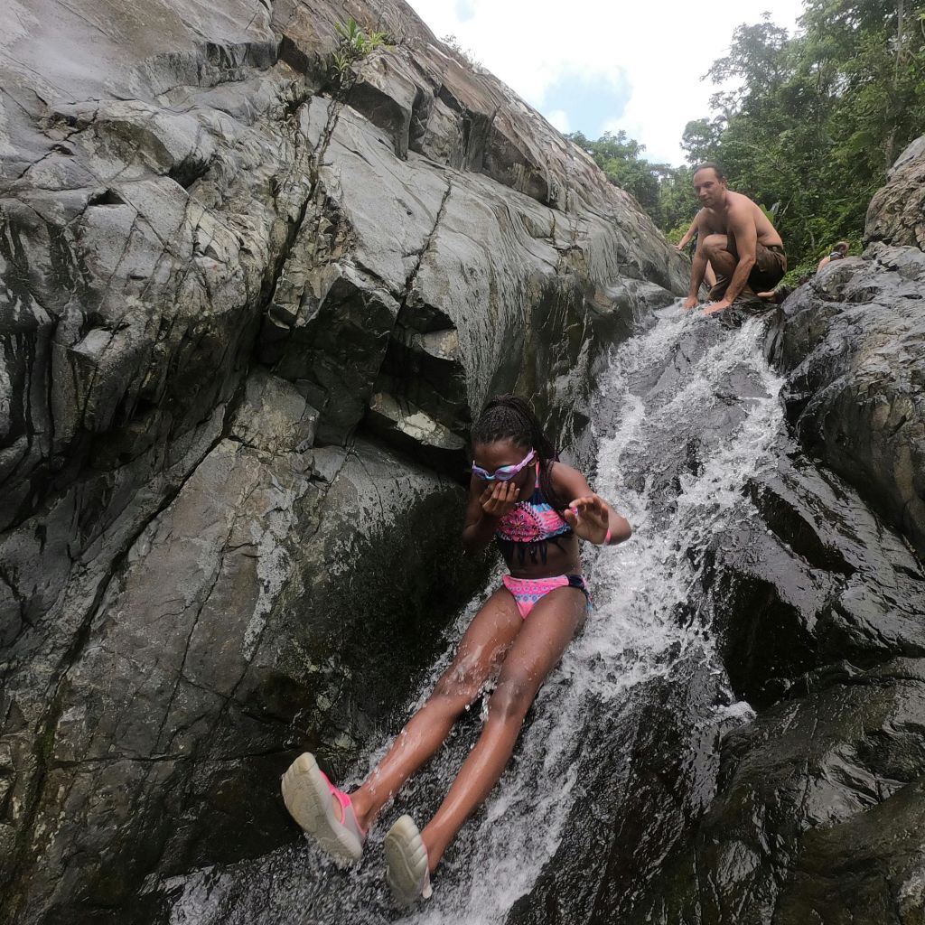 한 소녀가 바위 폭포를 따라 미끄러지듯 내려가고 한 남자가 맨 꼭대기에 쭈그리고 앉아 다음으로 미끄러질 준비를 합니다.