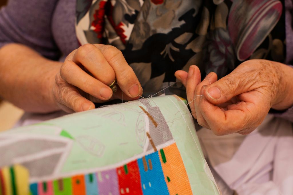 무늬가 있는 스카프를 두른 채 바늘과 실로 화려한 천을 꿰매는 사람의 손.