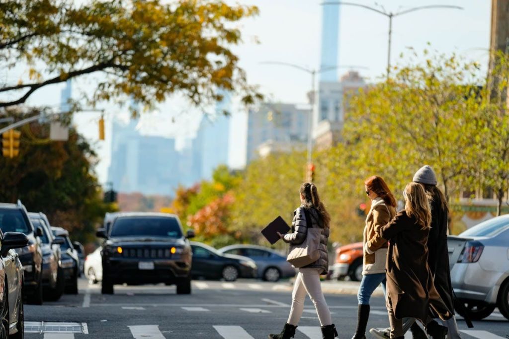 나무와 주차된 차량을 배경으로 횡단보도에서 도시 거리를 가로지르는 사람들.