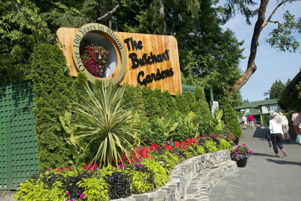 울창한 녹음과 화려한 꽃으로 둘러싸인 부차트 정원의 입구 표지판. 방문객은 배경에서 볼 수 있습니다.