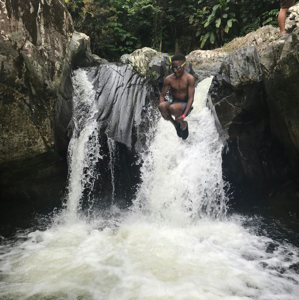 바위와 울창한 녹음으로 둘러싸인 폭포 수영장에 뛰어드는 사람.
