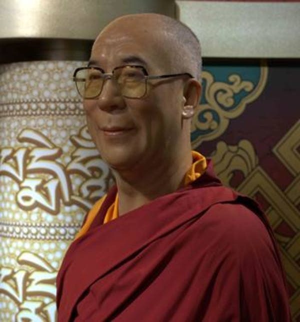 파란색과 노란색 패턴의 배경으로 손을 닮은 빨간색 조각상을 들고 웃고 있는 두 사람.