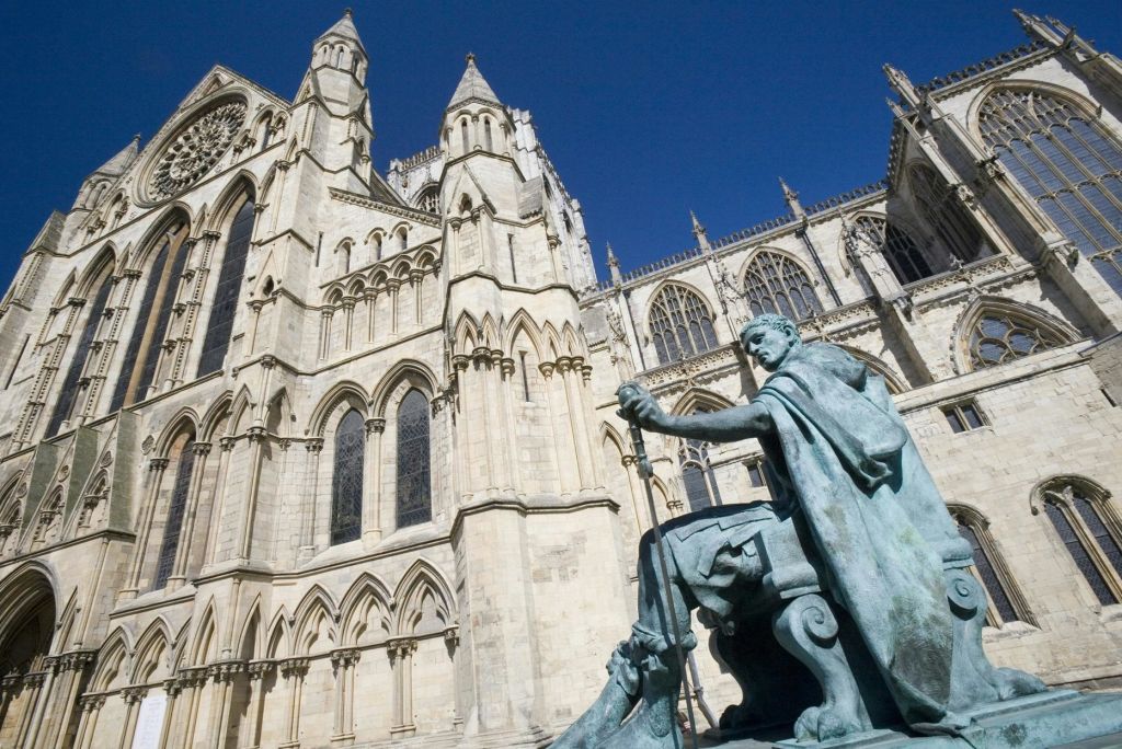 맑고 푸른 하늘 아래 커다랗고 화려한 고딕 양식의 대성당 앞에 칼을 들고 앉아 있는 모습의 조각상.