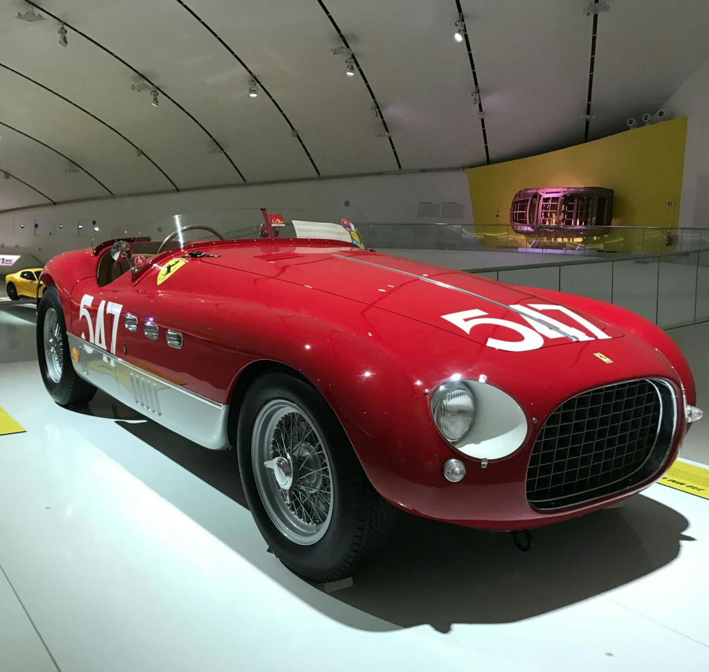 후드와 측면에 517이라는 숫자가 새겨진 빨간색 빈티지 레이스 카는 곡선형 천장이 있는 조명이 밝은 쇼룸에 전시되어 있습니다.