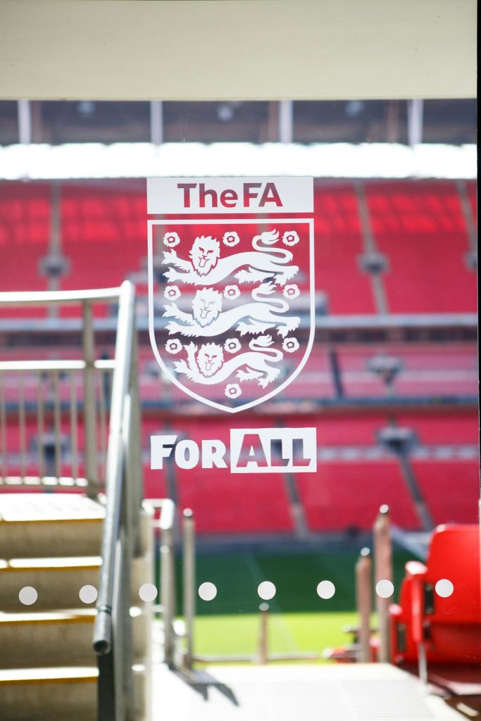 "The FA For All" 텍스트가 있는 유리 패널, 세 개의 사자 엠블럼, 유리를 통해 볼 수 있는 빨간색 경기장 좌석.