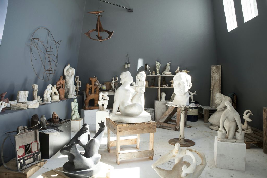 사람의 형상, 추상적인 형상, 가슴 등 다양한 조형물이 테이블과 선반에 배치된 스튜디오입니다.