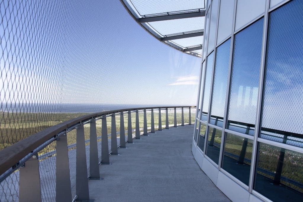 유리벽이 있는 고층 건물의 곡선형 통로와 먼 풍경이 내려다보이는 메쉬 안전 장벽.