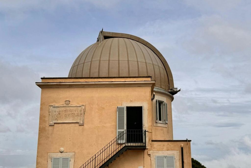 돔 모양의 커다란 지붕, 두 개의 닫힌 창문, 금속 계단이 있는 열린 문, 벽에 명판이 있는 건물.