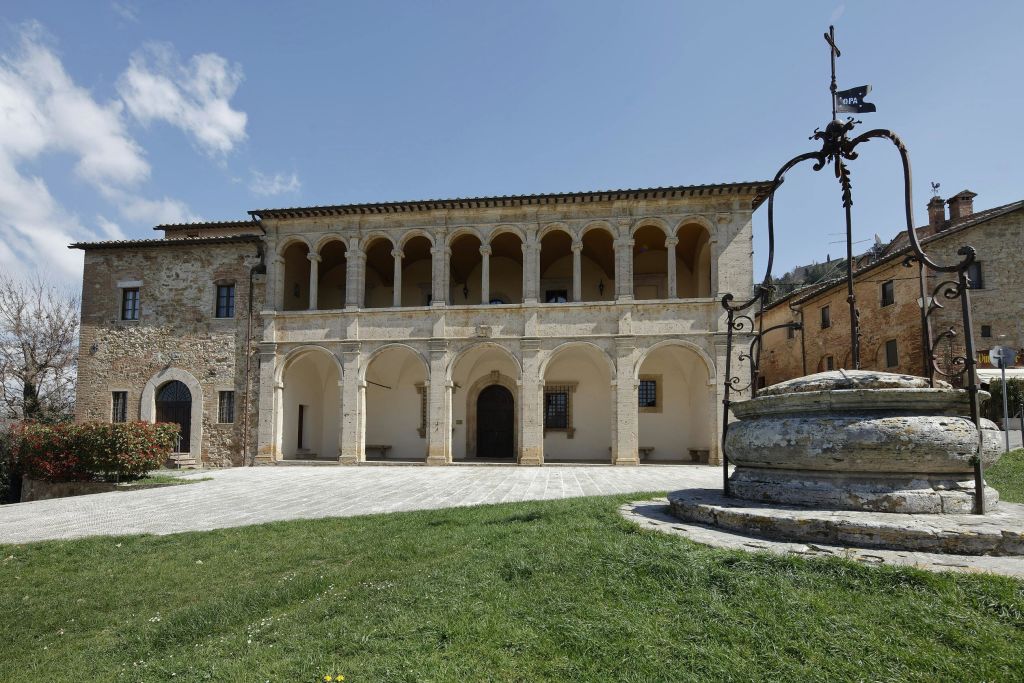 아치형 콜로네이드가 있는 역사적인 건물, 전경의 우물, 맑고 푸른 하늘 아래 잔디가 우거진 마당.