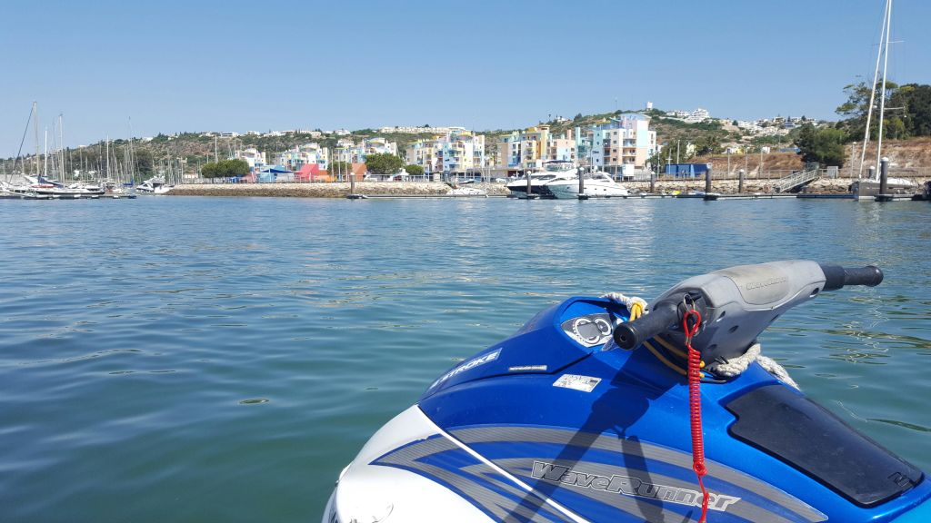 보트와 화려한 건물을 배경으로 선착장 근처의 물 위에 떠 있는 파란색과 흰색의 제트 스키. 위쪽의 맑고 푸른 하늘.