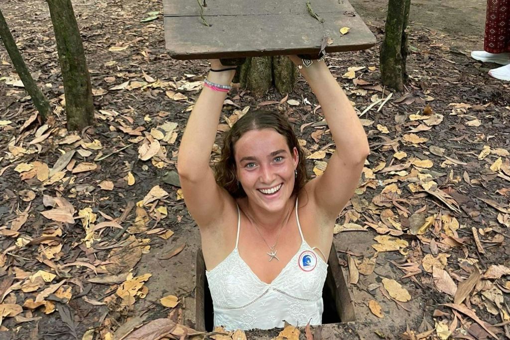 땅굴에서 나온 사람이 낙엽이 떨어진 숲 속에서 머리 위로 나무 덮개를 들고 미소를 짓고 있습니다.