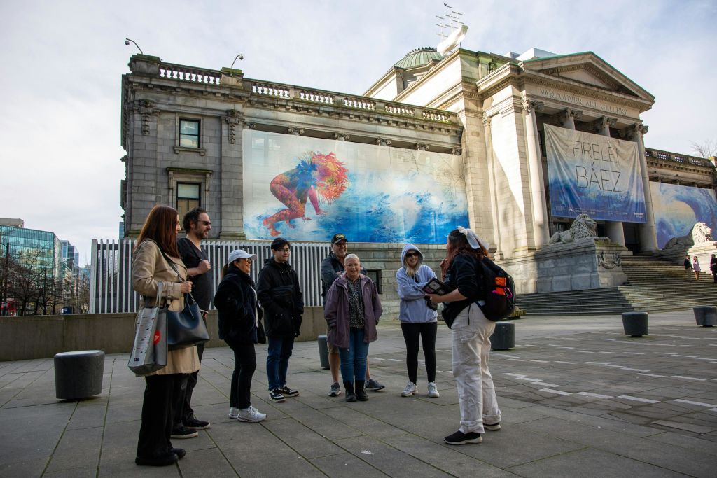 한 무리의 사람들이 커다란 벽화가 있는 오래된 건물 앞에 모여 물속에서 헤엄치는 사람을 묘사했습니다.