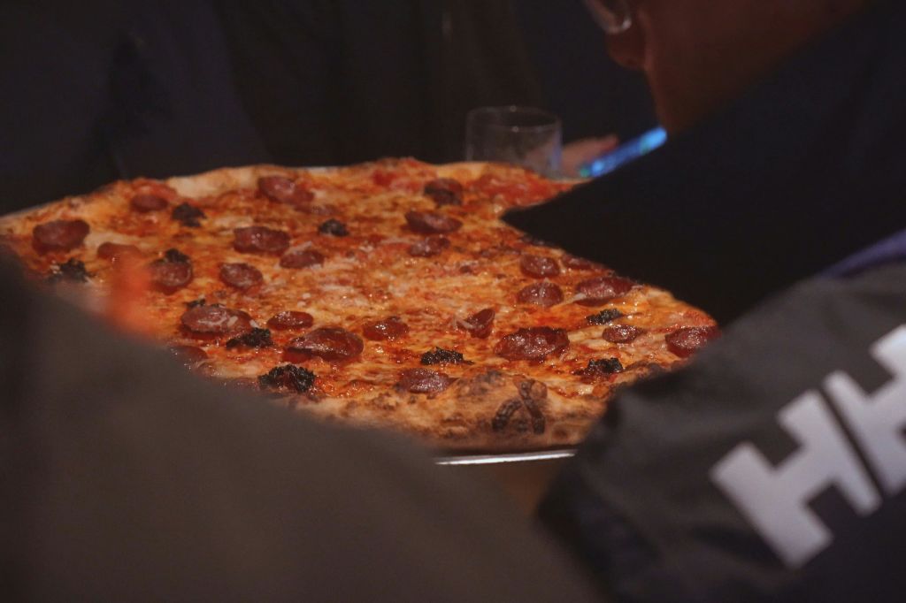 흐릿한 형상과 유리잔이 배경으로 제공되는 페퍼로니 피자의 클로즈업.