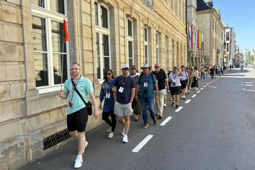 붉은 깃발을 든 투어 가이드가 커다란 창문이 있는 건물 옆 거리를 따라 일행을 안내합니다.