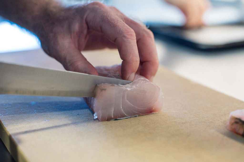 생선 조각을 도마에 칼로 썰어 넣는 손.