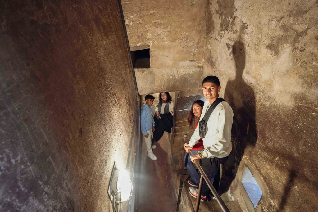 돌담이 있는 낡고 좁은 계단에 네 명이 서서 미소를 지으며 카메라를 올려다보고 있습니다.