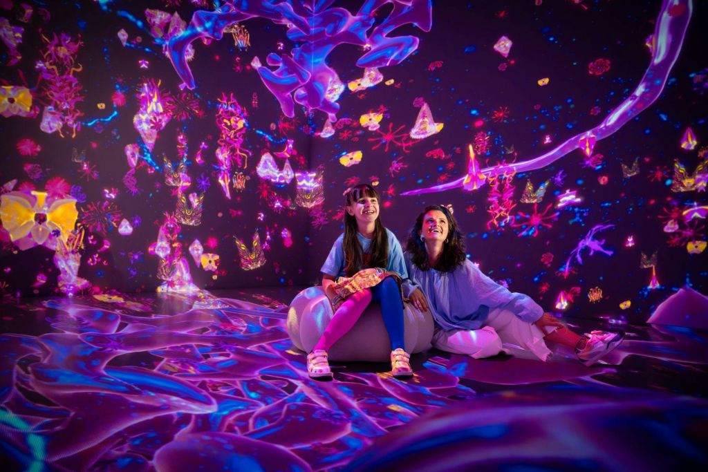 밝은 조명과 추상적인 디자인으로 가득한 다채롭고 몰입감 넘치는 디지털 아트 작품에서 두 사람이 미소를 짓고 있습니다.