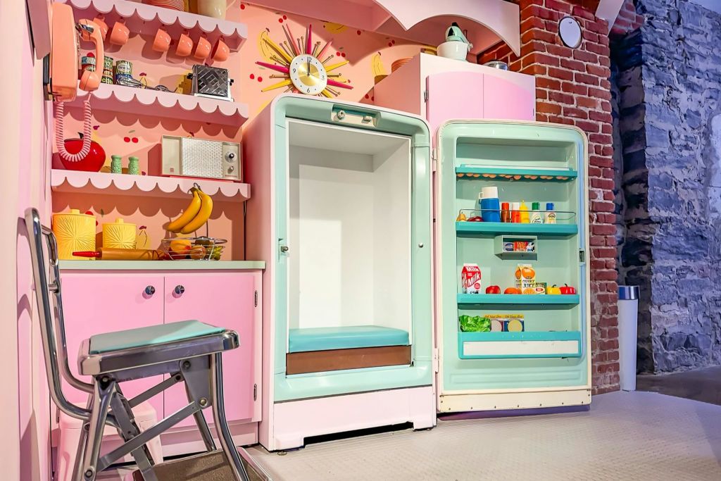 분홍색 테마의 복고풍 주방으로, 음식으로 채워진 개방형 빈티지 냉장고와 빈 냉동고가 특징입니다.