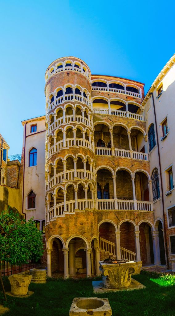 맑고 푸른 하늘을 배경으로 여러 개의 아치, 발코니, 기둥이 있는 나선형 계단이 있는 역사적인 건물입니다.