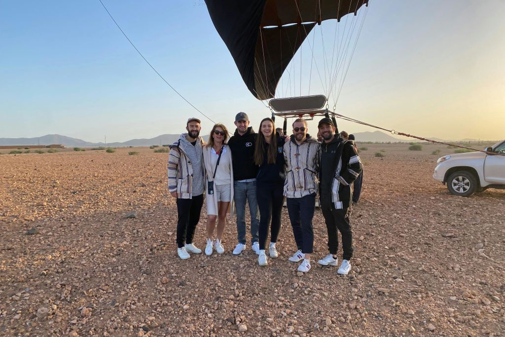 열기구의 일부가 보이는 바위밭에 여섯 명이 함께 서 있습니다.