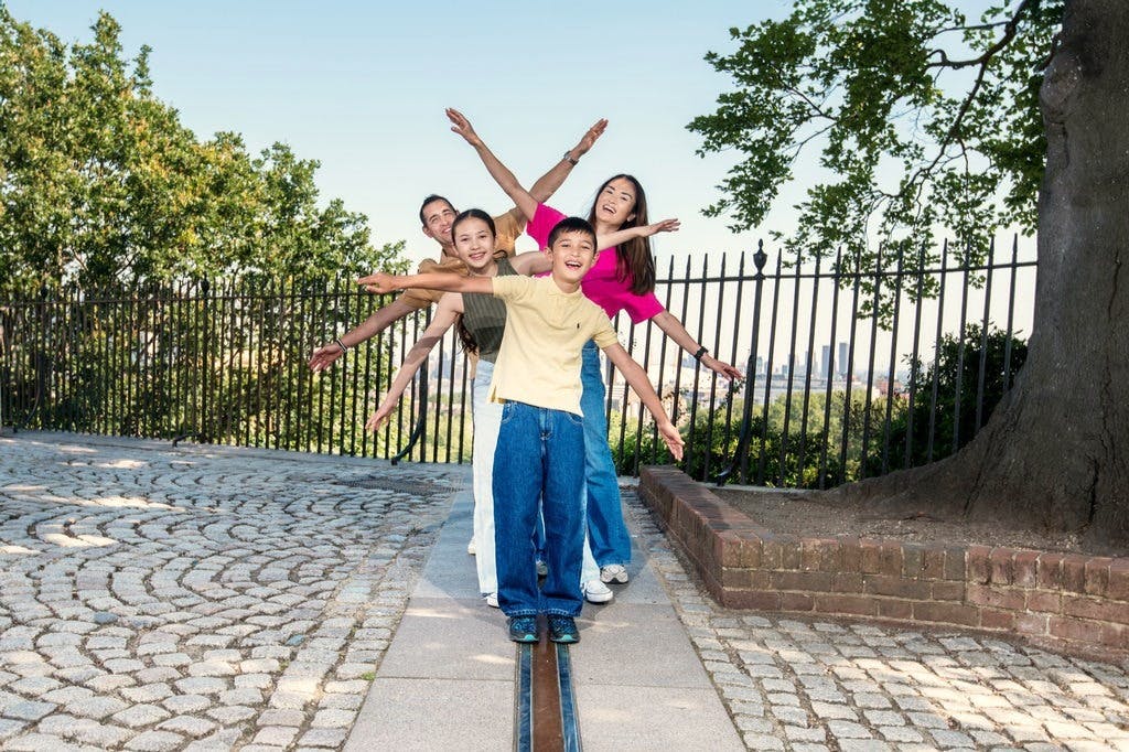 자갈길과 나무가 있는 공원의 울타리 옆에서 팔을 뻗고 웃으며 포즈를 취하는 네 사람이 줄을 잇고 있습니다.