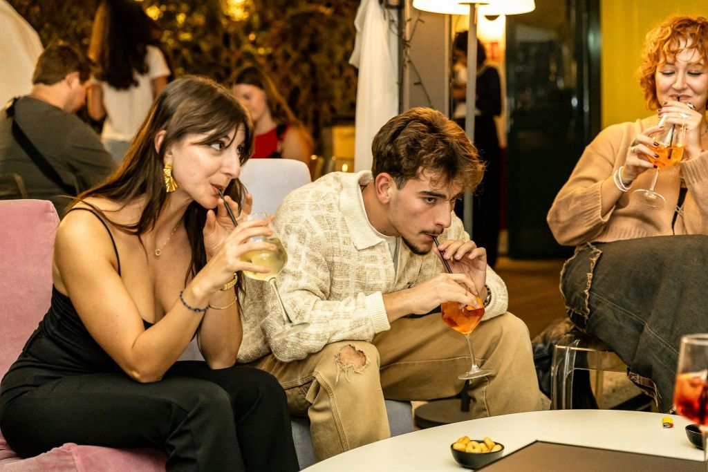 따뜻한 조명이 있는 캐주얼한 실내 환경에서 세 사람이 함께 앉아 잔에 음료를 들고 있습니다.