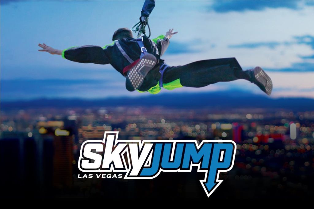 흐릿한 도시 풍경을 배경으로 플랫폼에서 뛰어내리는 하네스를 입은 사람. "SKYJUMP LAS VEGAS" 텍스트 오버레이.