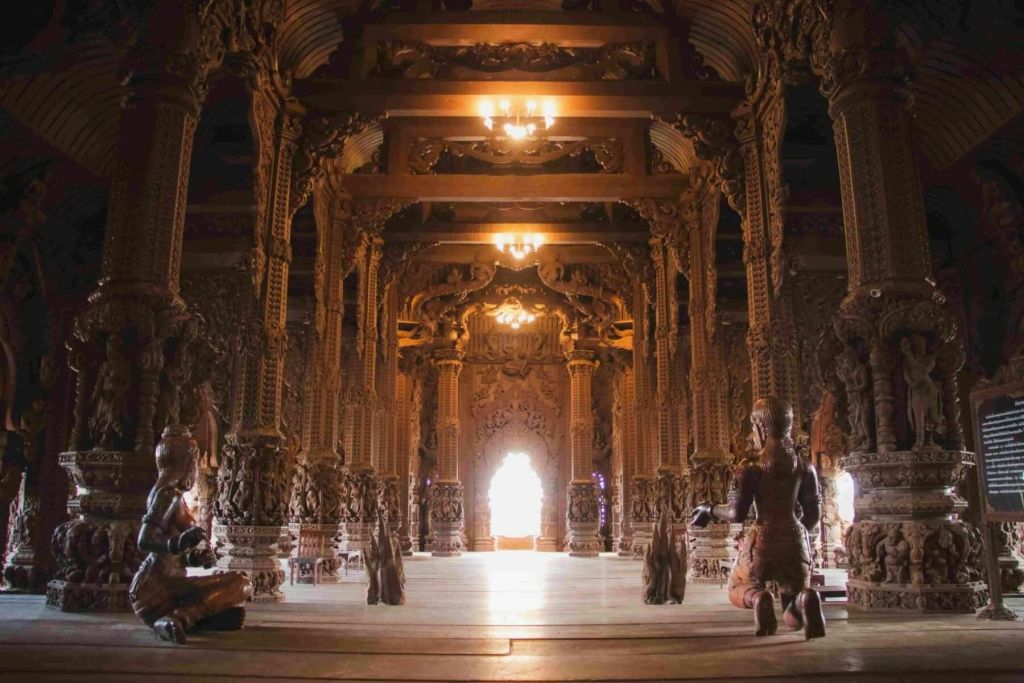정교한 기둥과 샹들리에, 무릎을 꿇은 모습으로 화려하게 조각된 목조 사원 내부.