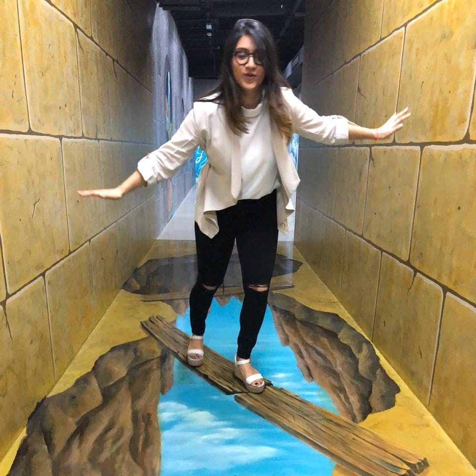 한 여성이 광학 착시 전시물에서 나무 판자의 사실적인 바닥 그림과 아래쪽 협곡의 물의 균형을 맞추고 있습니다.