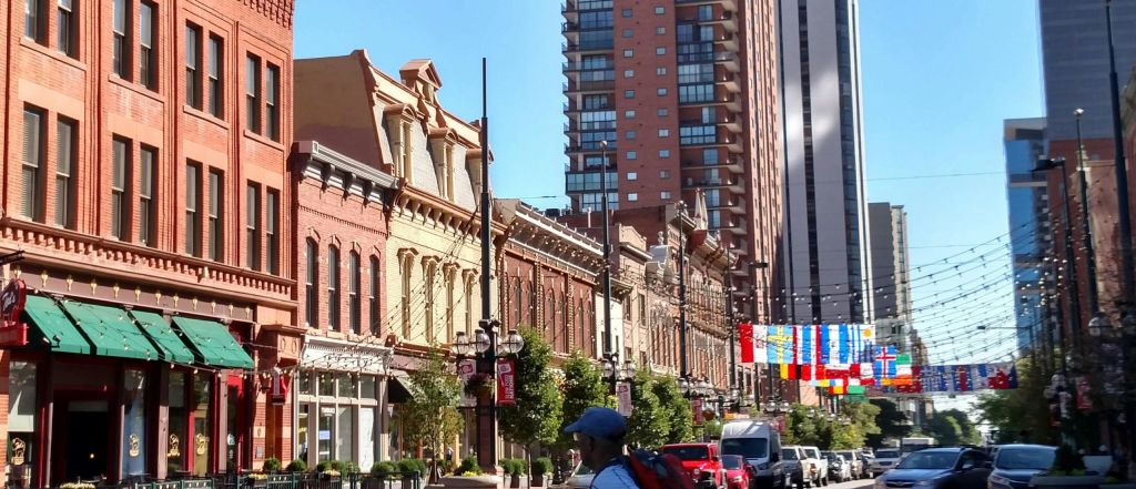 역사적인 벽돌 건물, 나무, 매달린 조명, 보행자, 현대적인 고층 건물을 배경으로 한 도시 거리입니다.