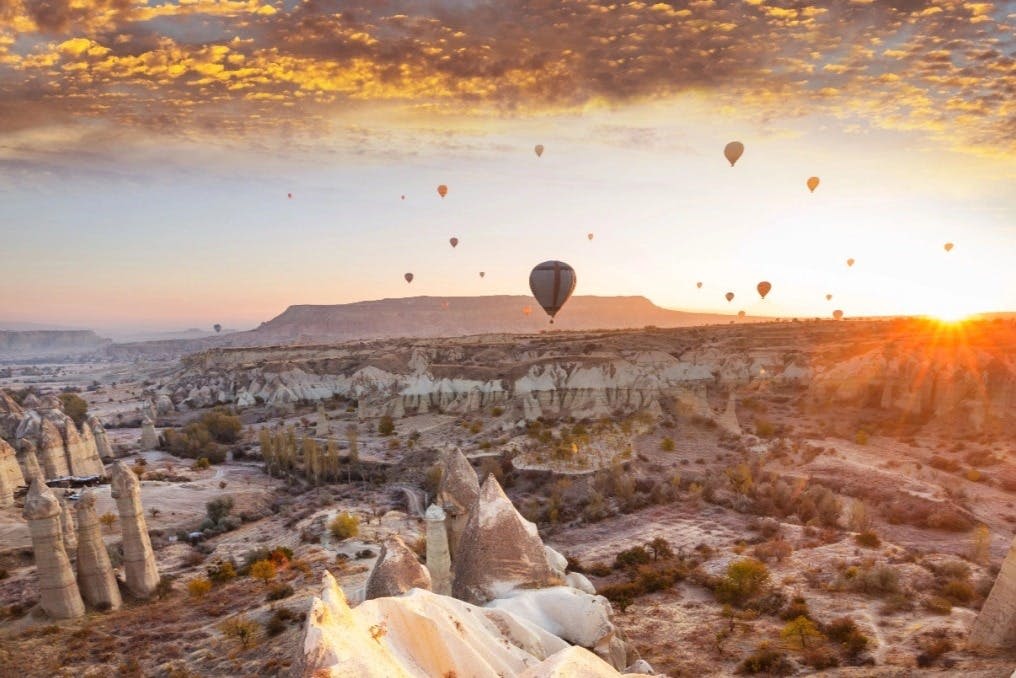 해가 질 무렵 바위 위에 떠 있는 열기구와 흩날리는 구름으로 가득 찬 하늘.
