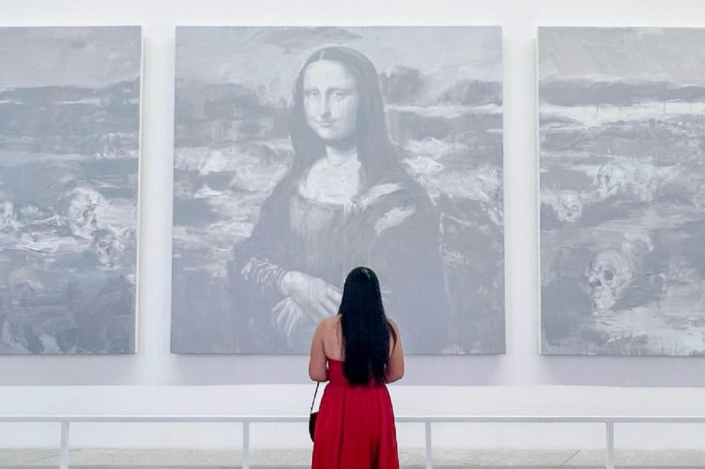 갤러리의 모나리자를 닮은 회색조 작품 앞에 빨간색 드레스를 입은 사람이 서 있습니다.