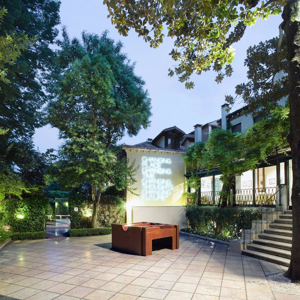 나무가 있는 야외 안뜰, 계단, 나무 테이블, 조명 텍스트가 투영된 벽.