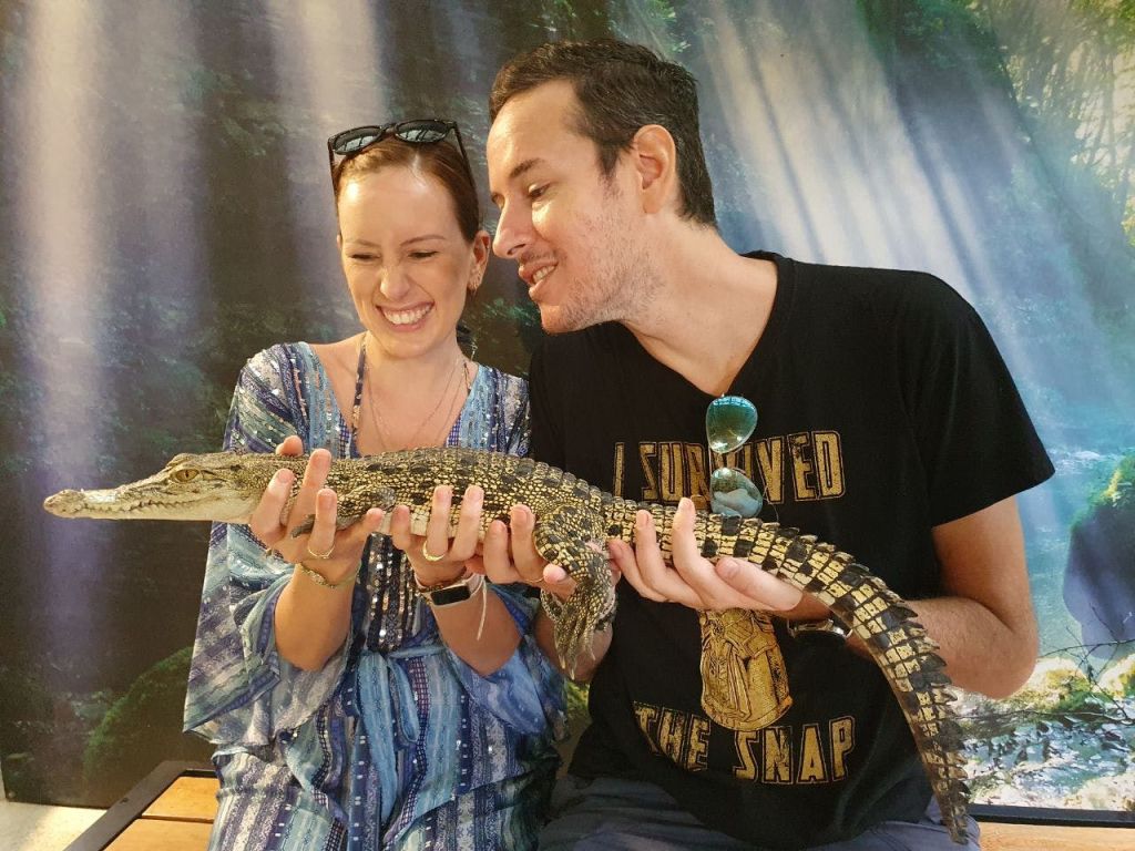 숲을 배경으로 작은 악어를 사이에 두고 웃고 있는 두 사람.