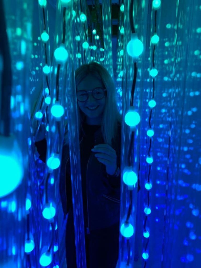 안경을 쓴 사람이 어둡고 분위기 있는 공간에 걸려 있는 수많은 파란색 LED 조명 사이에 서 있습니다.