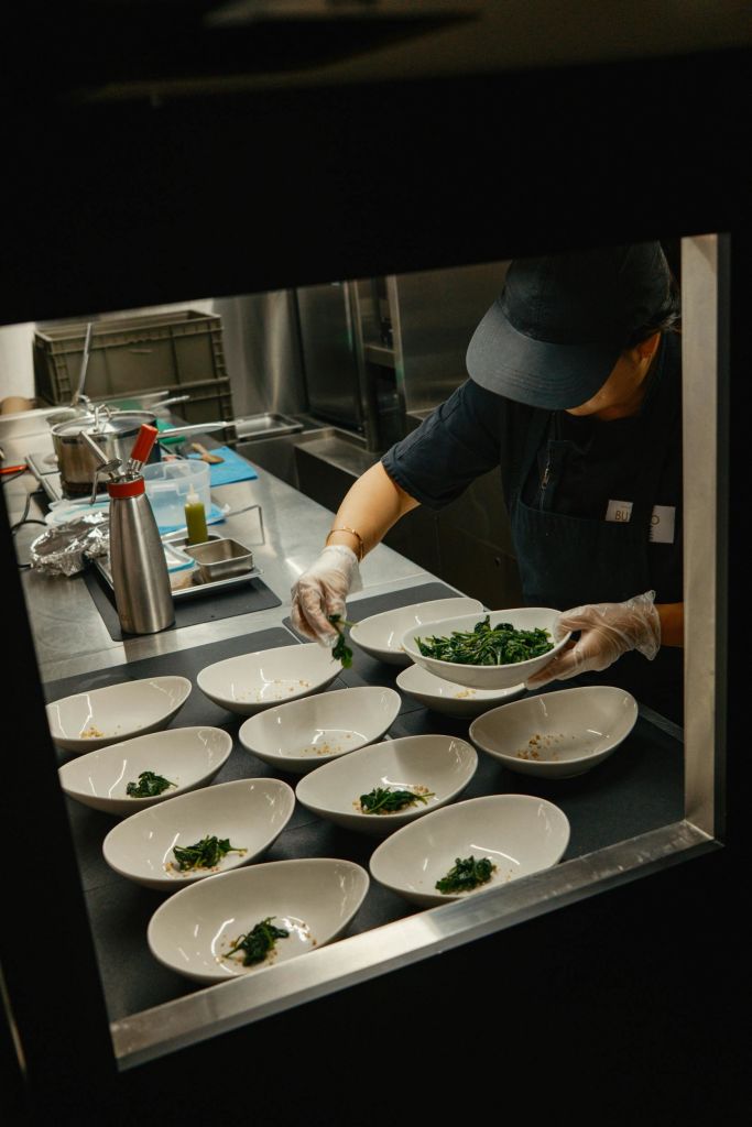 주방에서 그릇, 식기, 주방용품으로 둘러싸인 채소가 담긴 접시를 만드는 셰프.