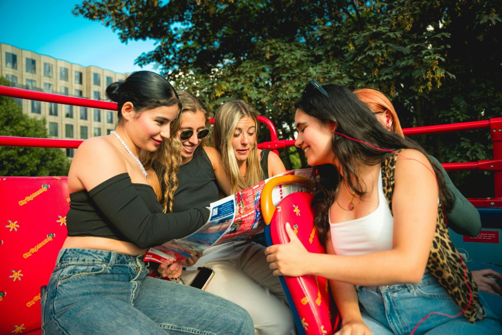 한 무리의 여성들이 야외에 앉아 나무와 건물을 배경으로 형형색색의 지도를 함께 보고 있습니다.