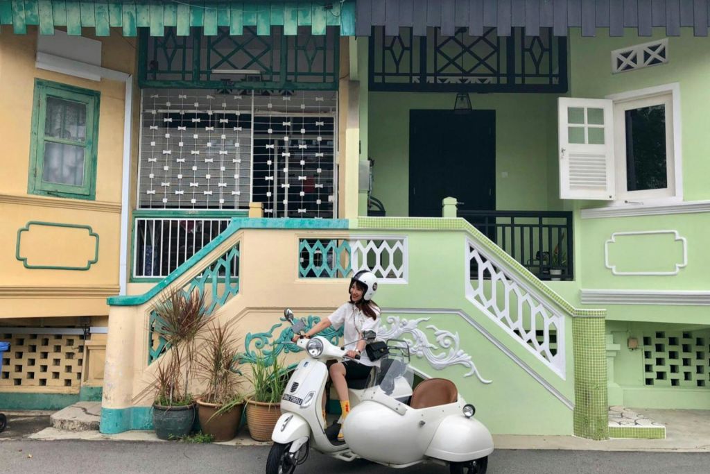 녹색으로 강조된 화려한 색상의 집 앞에는 사이드카가 달린 흰색 전동 스쿠터에 헬멧을 착용한 사람이 앉아 있습니다.