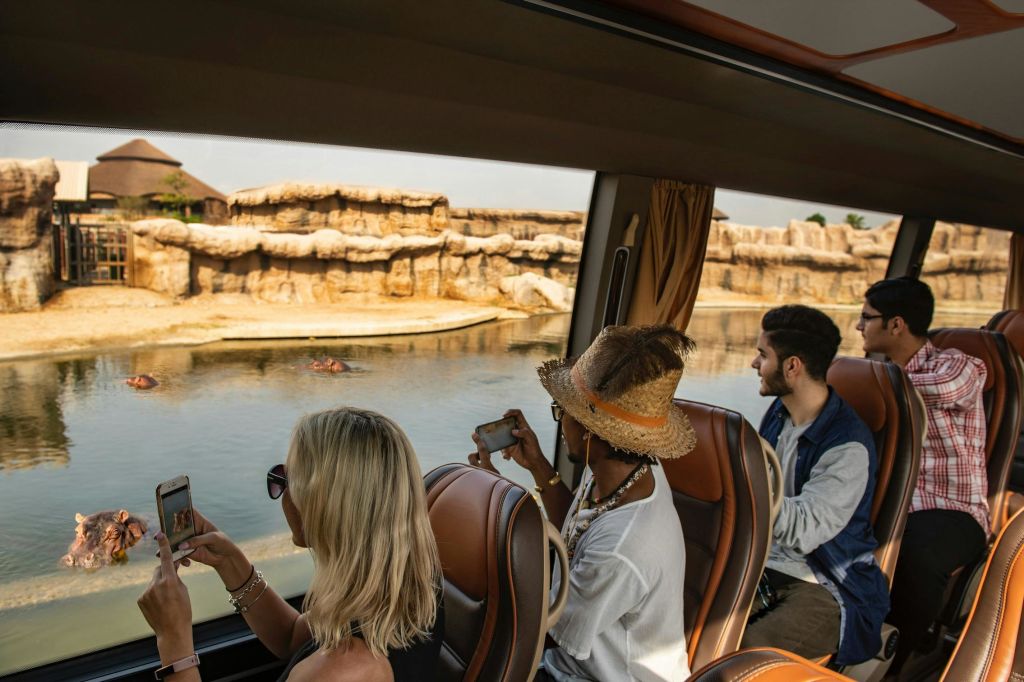 세 사람이 버스에 앉아 물과 바위가 가득한 풍경을 바라보고 있습니다.