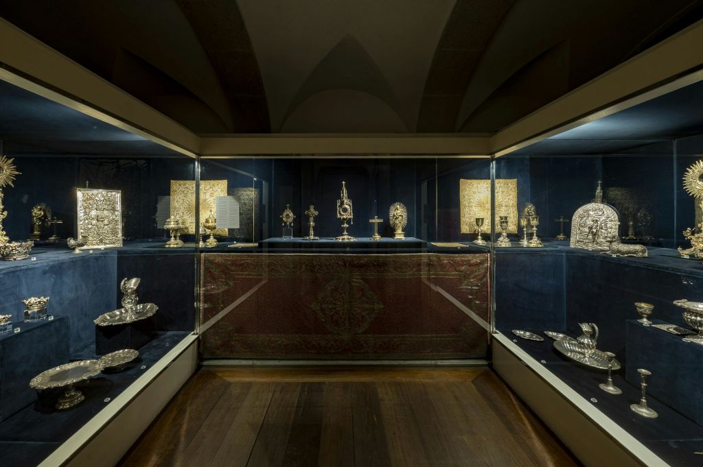 박물관 환경에서 부드러운 조명으로 비춰지는 블루 벨벳의 은색 종교 유물을 보여주는 유리 디스플레이 케이스.