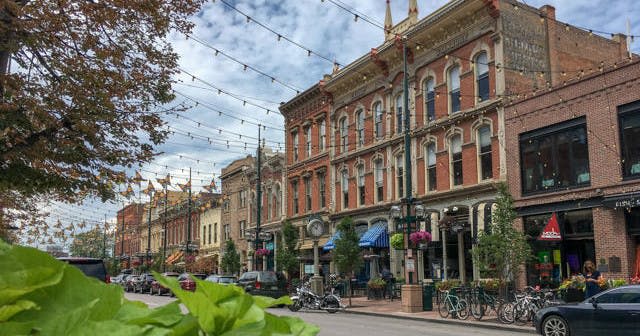 유서 깊은 벽돌 건물, 매달려 있는 조명, 상점가, 주차된 차량이 있는 거리 풍경은 흐린 날 일부를 볼 수 있습니다.