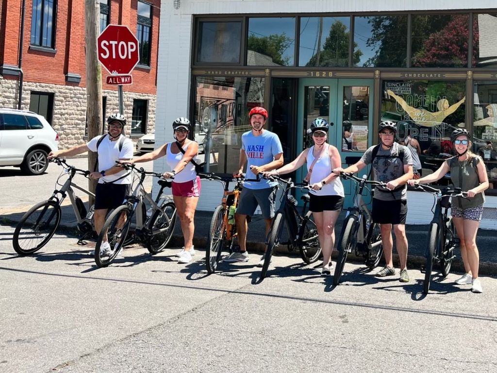 화창한 날 상점 앞 거리에 자전거를 탄 사람들이 서 있습니다.