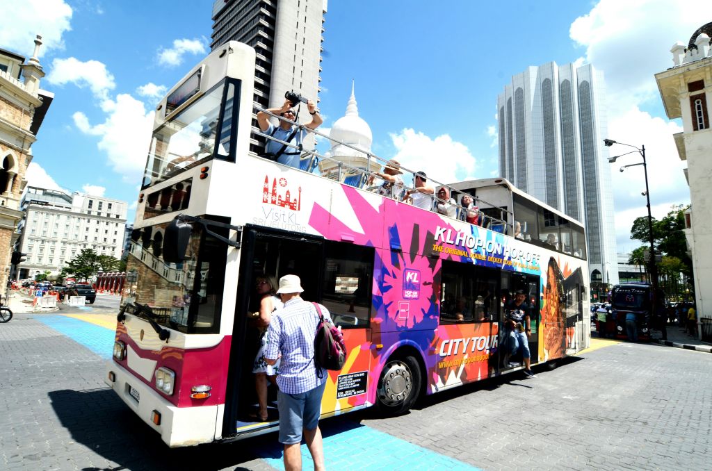 화창한 날 현대식 건물을 배경으로 다채로운 색상의 2층 시티 투어 버스에 탑승하고 앉아 있는 관광객들.