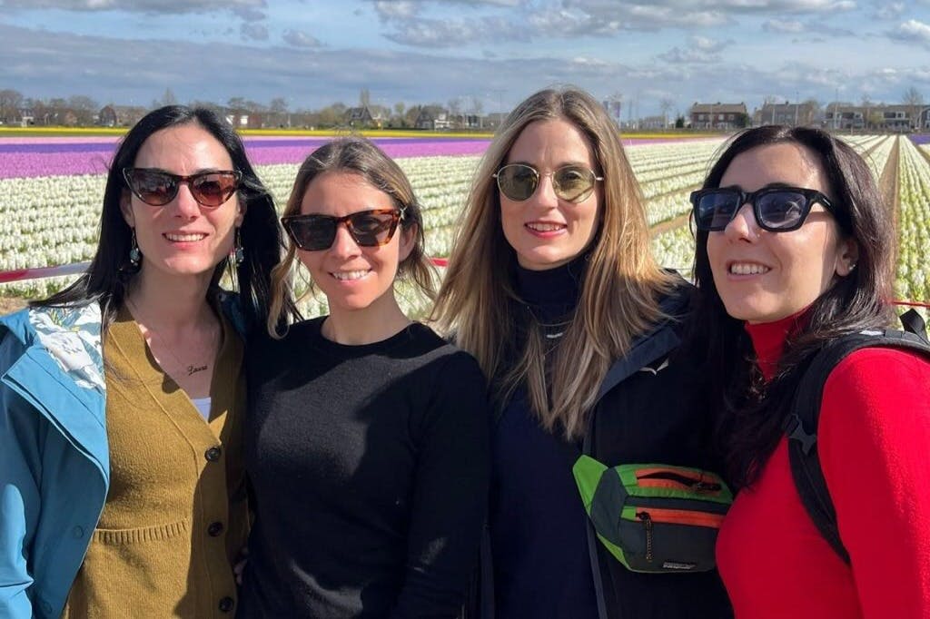 부분적으로 흐린 하늘 아래 화려한 튤립밭 앞에 선글라스를 쓴 세 명의 여성이 서 있습니다.