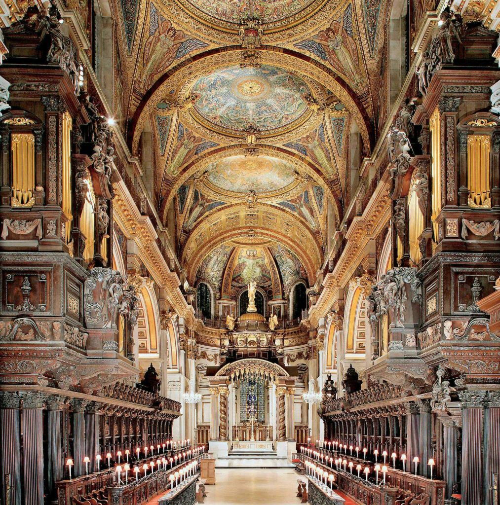 풍성하게 장식된 아치형 천장, 정교한 목조 성가대, 통로를 따라 불이 켜진 촛불이 있는 호화로운 교회 내부.
