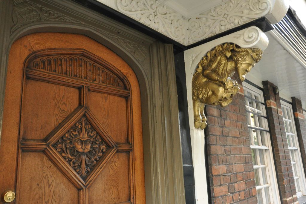 금염소 조각과 디테일한 흰색 몰딩이 특징인 장식 코너 옆에 정교한 조각이 있는 나무 문입니다.