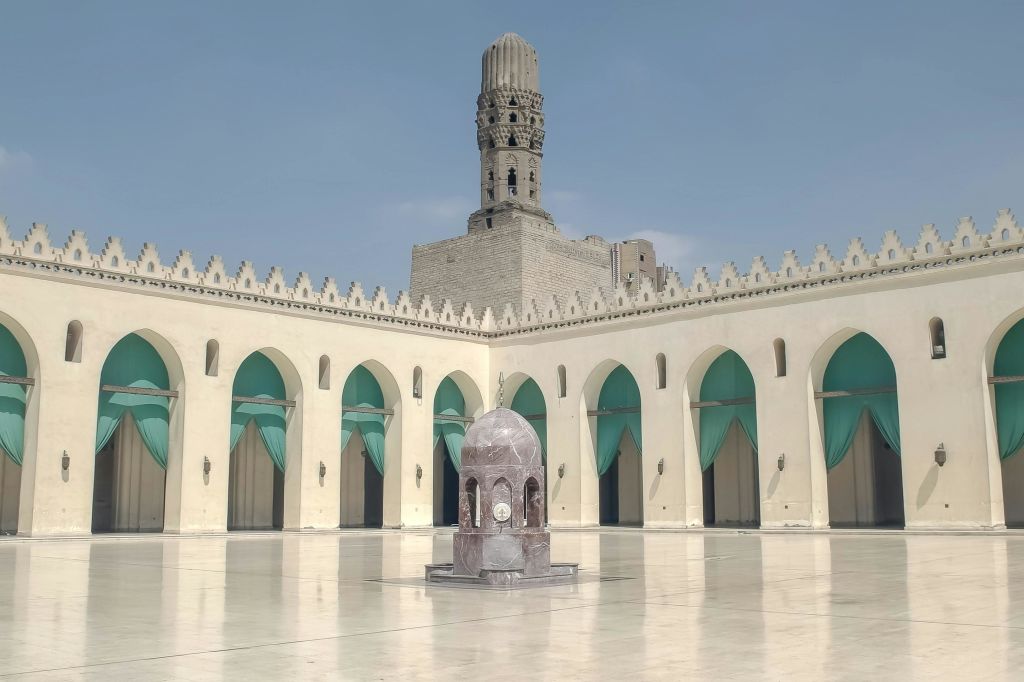 아치형 출입구로 둘러싸인 중앙 분수대와 높고 화려한 미나레트를 배경으로 마당이 펼쳐집니다.