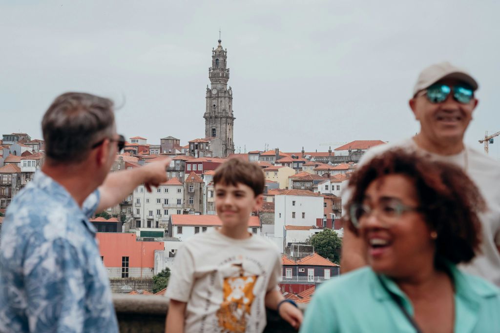 높은 시계탑을 배경으로 도시 풍경 앞에 서 있는 한 소년과 두 명의 어른이 미소를 짓고 있습니다.