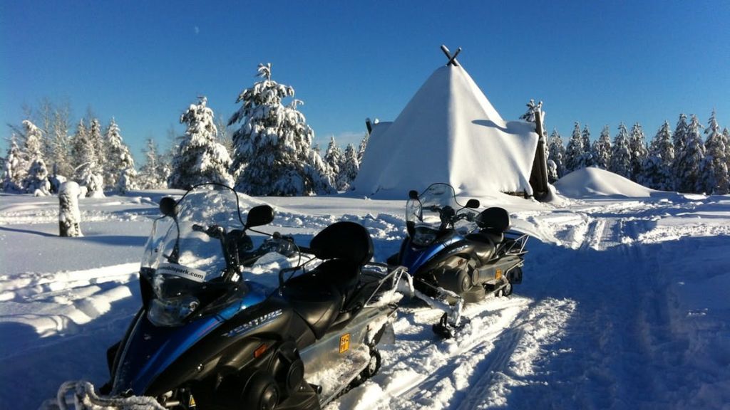 맑고 푸른 하늘 아래 눈이 쌓인 나무가 있는 눈 덮인 풍경의 텐트 앞에 주차된 두 대의 스노모빌.